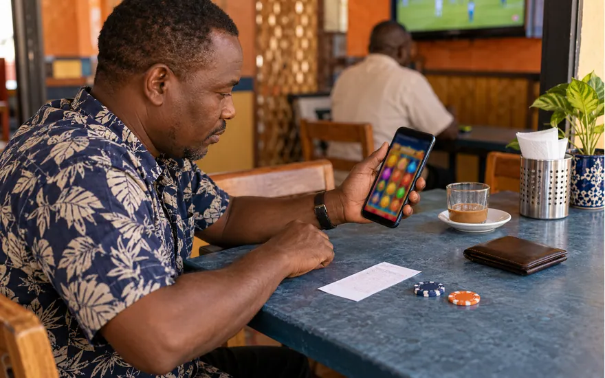 Adult in Tanzania holding a phone with abstract slot reels beside a betting ticket